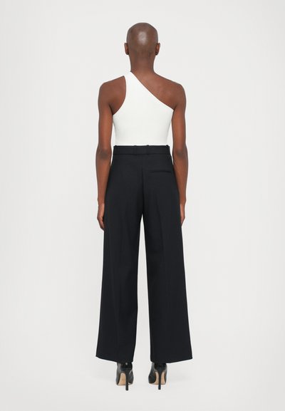 White ribbed one-shoulder top paired with high-waisted, wide-leg black trousers. Black high-heeled shoes complete the outfit.