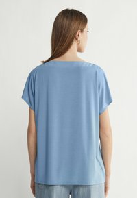 Ljusblå kortärmad topp med avslappnad passform och rund halsringning. Mjuk tyg. Bakifrån visas en enkel design utan synliga mönster eller detaljer.