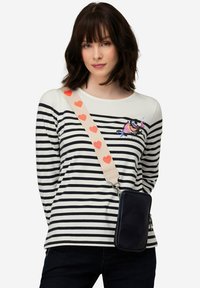 Granatowa torebka crossbody o fakturze z sercem na pasku; modelka nosi koszulę w paski w różowo-czarną kolorystykę z haftowanym wzorem.