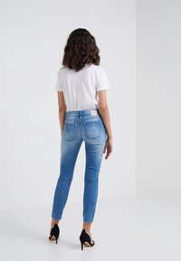 Úzké džíny z denimu, s vybledlou modrou barvou, vysokým pasem a designem s pěti kapsami, v kombinaci s bílým tričkem a černými podpatky.