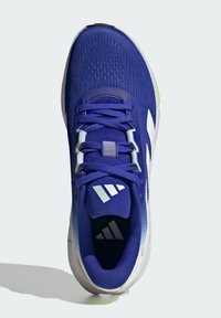 Blauer Sportschuh mit einem strukturierten Mesh-Obermaterial, weißen Akzenten, gepolstertem Zungenbereich und einer rutschfesten Sohle mit grünen Highlights. Verstellbare Schnürsenkel inklusive.
