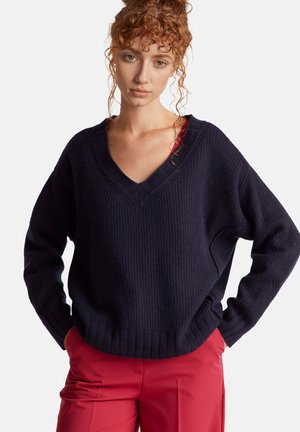 Maglione lavorato a maglia di un blu scuro, con scollatura a V, texture a coste e vestibilità comoda. Abbinato a pantaloni rossi sartoriali con gamba dritta.