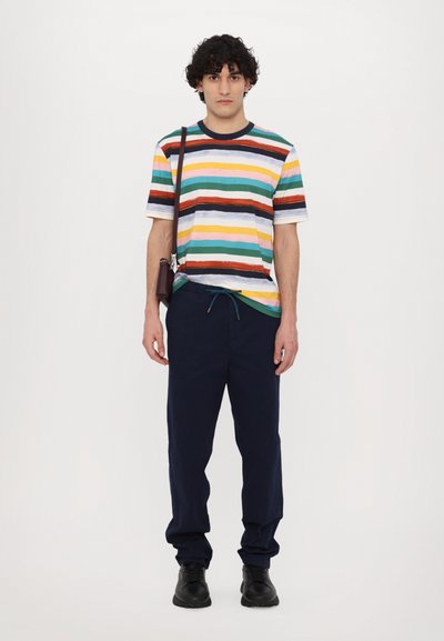 Tricou cu dungi orizontale multicolore, asociat cu pantaloni bleumarin. Pantofi negri și o geantă mică de umăr maro.