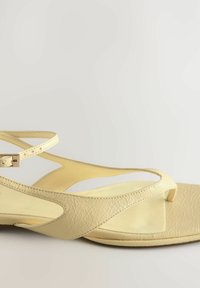 Sandalele cu brâu subțire de culoare galbenă prezintă un superior texturat din material sintetic, un design minimalist și o talpă plată cu o curea subțire la gleznă.