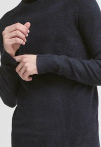 Tamno plavi pulover od meke, teksturirane vune s dodatkom, koji ima duge rukave i rebraste manžete, s opuštenim krojem oko trupa.