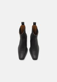 Botas de tobillo de cuero negro con punta afilada, paneles laterales elásticos y forro marrón. Cuentan con una suela de goma plana para mayor estabilidad.