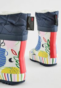 Bottes de pluie en caoutchouc colorées avec un dessus matelassé bleu marine, des motifs floraux, des accents rouges et des semelles rayées. Doublées de matériau doux et moelleux.