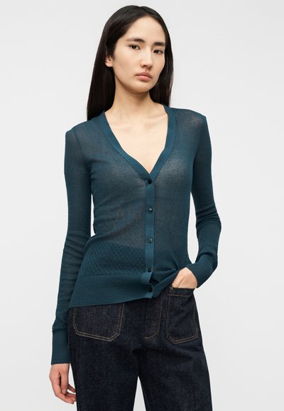 Τυρκουάζ ελαφρύ ζακέτα με λαιμόκοψη σε σχήμα V, μακριά μανίκια και κουμπιά εμπρός. Διαθέτει υφή με ανάγλυφο μοτίβο και ριμπ μανσέτες και τελείωμα.