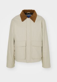 Chaqueta beige hecha de tela texturizada, con un cuello de pana marrón, dos bolsillos frontales y un diseño de corte recto.