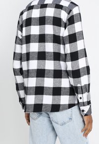 Svart- och vitrutigt flanellskjorta med lång ärm och knappdetaljer, i kombination med ljusblå denimjeans. Texturerad tyg.