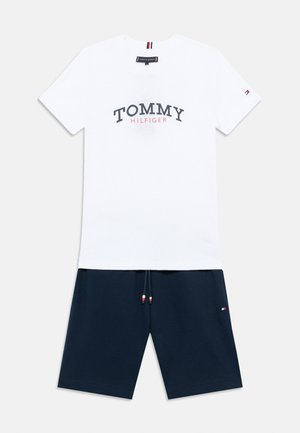 Valge puuvillane t-särk, millel sinise ja punase kirjaga kiri "TOMMY HILFIGER". Ühildatud tumesiniste lühikeste pükstega, millel on pael, millel on punased, valged ja sinised aktsendid.