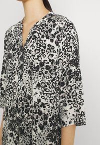 Blouse ample en tissu léger, dotée d'un motif léopard monochrome avec des couleurs noir, gris et blanc. Col à revers, manches courtes.