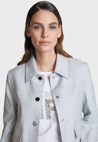Gray jacket with a collared neckline, double-breasted fastening, and two front pockets. Fabric has a smooth texture with subtle detailing.