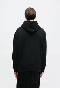 Hanorac negru cu glugă, cu o croială relaxată, manșete și tiv cu reiat. Textură netedă, design minimalist, fără logo-uri vizibile.