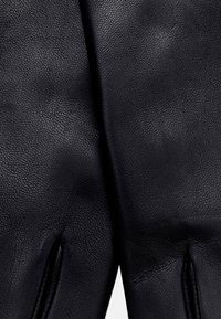 Schwarze Lederhandschuhe mit einer strukturierten Oberfläche, die ein elegantes Design und eine maßgeschneiderte Passform aufweisen, mit dezenten Nähdetailierungen.