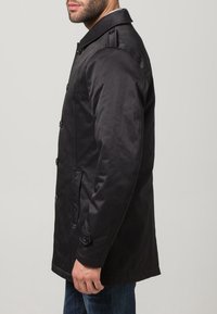 Svart vattentålig jacka med knäppning fram, dubbla sidofickor och axelklaffar på axlarna. Slät, matt textur.