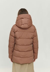 Brown puffer jacket with a hood, featuring a quilted design, soft texture, and prominent stitching. Worn over a beige skirt.