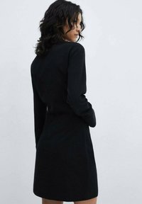 Zwart lange mouw jurk met een aansluitend ontwerp en een lichte flare aan de zoom. Gemaakt van gladde stof met minimale details.