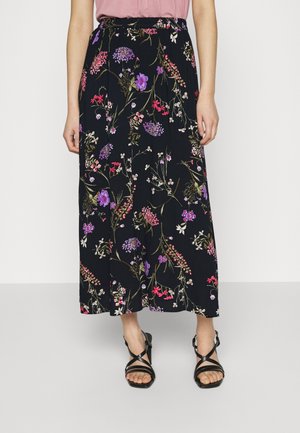Jupe longue fleurie présentant un fond noir avec des fleurs multicolores, une taille élastique et un design fluide. Associée à des sandales noires à brides.