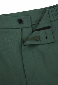 Pantalons verts avec fermeture à bouton et zip. Pas de motifs visibles, présentant une texture lisse et une taille élastique pour plus de confort.