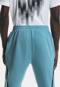Gros plan sur une personne portant un pantalon bleu clair avec une ceinture élastique et un t-shirt blanc à motif pixelisé noir.