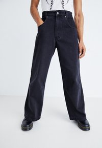 Černé džíny s širokým střihem a vysokým pasem, se předními kapsami, zapínáním na knoflíky a mírným vyblednutím. V kombinaci s černými platformovými botami.