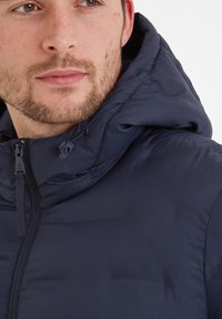 Navy blue padded jacket with a hood, featuring a front zipper, elastic drawstrings, and a smooth texture across material.