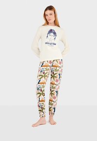Crème lange mouwtop met blauwe grafische details, gecombineerd met gestreepte broek met bloemen, palmbomen en vlinders. Zachte stoftextuur.