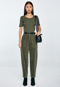 Olivově zelený žebrovaný top s krátkými rukávy, vysoké kordové kalhoty s předními kapsami a černé kotníkové boty. Obsahuje černou crossbody tašku.