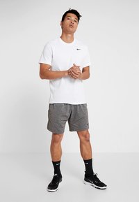 Meeste sportlik riietus: valge lühikeste varrukatega T-särk, hallid lühikesed püksid, mustad spordijalatsid ja mustad sokid, millel on kogu aeg Nike bränding.