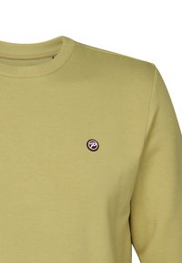 Sudadera de color verde oliva claro hecha de una tela suave, con un escote redondo y un pequeño logo circular bordado en el pecho.