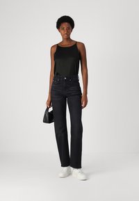 Jeans de mezclilla negros de cintura alta con un corte recto, combinados con una blusa sin mangas negra y zapatillas blancas, sosteniendo un bolso pequeño negro.