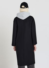 Cappotto lungo nero con cappuccio grigio, texture liscia, maniche larghe e design dritto. Presenta una cucitura posteriore e uno stile minimalista.
