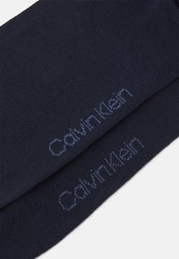 Sötétkék zoknik texturált kötött anyagból, a "Calvin Klein" márkanevével könnyebb kék fonallal hímezve.