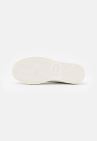 Vit sneakersula med herringbone-mönster, som har en platt, slät yta och en rektangulär varumärkespatch nära hälen.