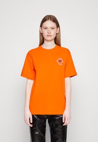 Oranje katoenen T-shirt met korte mouwen en een ronde halslijn, met een kleine grafische print op het linkerborstgebied.