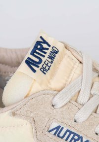 Sneaker beige con accenti in suede testurizzato, caratterizzato da una lingua color crema e etichettato con "AUTRY REELWIND" in cuciture blu navy.