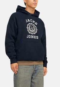 Sudadera azul marino con un bolsillo frontal, que presenta un diseño de logo y texto en blanco. Hecha de tela suave con un ajuste relajado y puños acanalados.