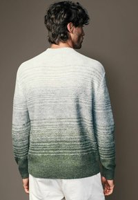 Suéter con un diseño de degradado que va de gris claro a verde oscuro, hecho de tejido texturizado con patrones de rayas horizontales y puños acanalados.