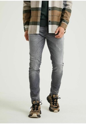 Jean skinny gris avec de légers détails usés, associé à une chemise à carreaux marron, vert et blanc. Complété par des baskets noires et marron.
