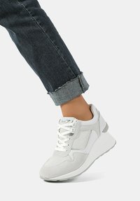 Sneaker bianco con una combinazione di materiali in rete e suede, caratterizzato da una tomaia texturizzata, punta rotonda e suola grigio chiaro.