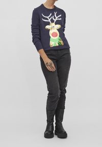 Pull en maille bleu marine avec un motif de renne en sequins dorés, verts et rouges, avec des bois blancs. Assorti à un jean noir et des bottes.