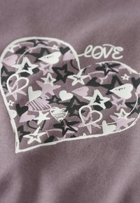 Un tissu violet présente un motif en forme de cœur rempli d'étoiles et de cœurs multicolores, avec le mot "amour" en blanc au-dessus de la forme du cœur.