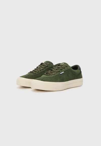 Adidași verzi din piele întoarsă, cu o talpă de cauciuc crem, vârf rotund, șireturi plate și un accent din piele neagră la călcâi. Design simplu și branding minimal.