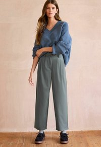 Maglione largo di colore azzurro chiaro con maniche testurizzate abbinato a pantaloni a vita alta e gamba larga di colore verde oliva e scarpe scure.