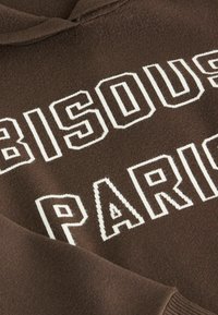 Felpa marrone con grande testo bianco "BISOU" e "PARIS", realizzata in tessuto morbido con una texture liscia e polsini a coste.