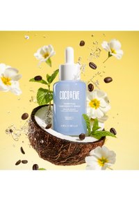 Tripeptid-Haarverdichtungsserum in einer hellblauen Glasflasche mit einer Pipette, umgeben von Kokosnussschalen, Blumen und Kaffeebohnen auf einem gelben Hintergrund.