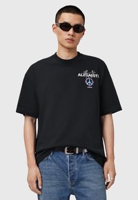 Sort oversized T-shirt i bomuld med et farverigt trykt logo med skeletter og fredssymbol på brystet. Bæres med blå jeans.