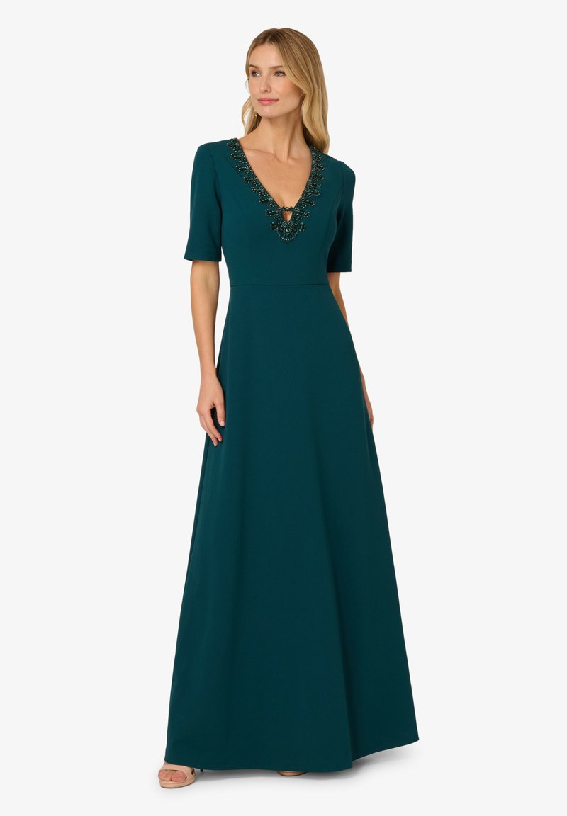 Tyrkysové maxi šaty s krátkými rukávy, hlubokým výstřihem do V a zdobením na límci korálky. Tkanina je hladká s pevným střihem.