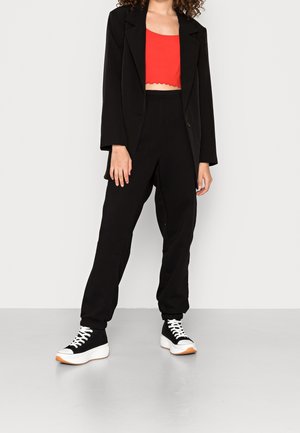 Person wearing a black blazer, red cropped top, black jogger pants, and black-and-white platform sneakers standing on a gray floor.